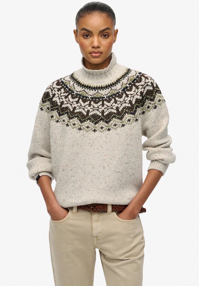 Pullover di maglina beige chiaro con collo alto, caratterizzato da un giogo decorato in marrone scuro, verde e bianco. Tessuto a trama continua con punteggiature.