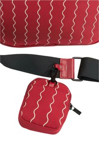 Červená taška s vlnitým bílým vzorem; obsahuje malou odnímatelnou kapsu a černý nastavovací popruh s kovovými prvky. Texturovaná tkanina.