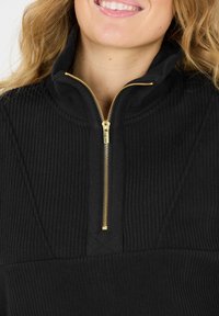 Schwarzer Zip-Pullover aus geripptem Stoff. Verfügt über einen goldfarbenen Reißverschluss und einen strukturierten Kragen. Glatte Textur mit subtilen Design-Details.