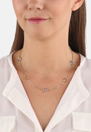 Złotonaś necklace z naprzemiennymi gładkimi i skręcanymi okrągłymi ogniwami. Projekt łańcucha zdobiony srebrnymi akcentami. Noszona przez osobę w białej koszuli.