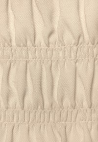 Ljusbeige tyg med en strukturerad, samlad mönstring med växlande släta och skrynkliga sektioner, vilket ger en dimensionell effekt.