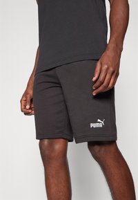 Svart shorts laget av en bomullsblandingsstoff, med et PUMA-logo i hvitt, en enkel, sydd kant og en avslappet passform.