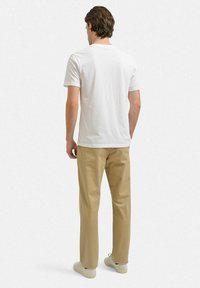 Hvid t-shirt med korte ærmer, parret med beige bukser og lyse sneakers. Stofudseendet er glat; snittet er afslappet og uformelt.
