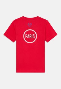 T-shirt en coton rouge avec un design circulaire blanc comportant le mot "PARIS" en gras. Logo Nike en bleu au niveau du col. Manches courtes, col rond.