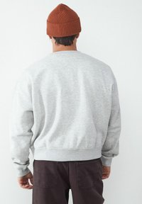 Szary polarowy sweatshirt z prążkowanymi mankietami i dołem, w połączeniu z teksturowaną brązową wełnianą czapką. Model odwrócony, ukazujący tylny wzór.