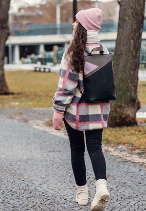 Schwarzer und rosa geometrischer Rucksack mit grauem Akzent, getragen zu einer karierten Wolljacke und einer rosa Mütze, kombiniert mit schwarzen Leggings und cremefarbenen Stiefeln.