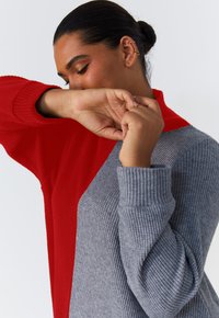 Pull en laine avec un design de blocs de couleurs rouge et gris. Présente une texture côtelée et des manches longues, avec un col haut et une coupe décontractée.