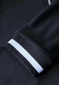 Svart sweatshirt-mudd med texturerad stickning, som har en vit och ljusblå randig detalj längs kanten. Slät tygfinish.