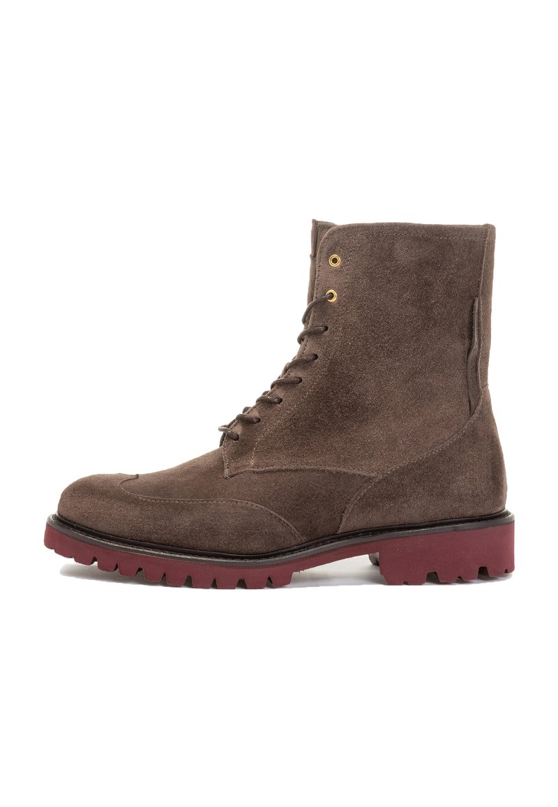 Brown suede ankle boot with a rounded toe, six metal eyelets, and a rugged red rubber sole. Features a smooth texture and clean design.