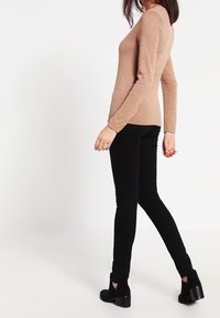 Beige långärmad topp med en figurnära design, mjuk textur och rund halsringning, i kombination med svarta slim fit-jeans och ankelstövlar.