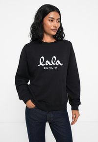 Čierna mikina z mäkkého materiálu s bielym logom, ktoré na prednej strane znie "lala BERLIN". Dlhé rukávy s rebrovanými manžetami.