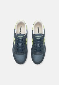 Sötétkék sneaker cipő világoszöld részletekkel, hálós és velúr anyagból készült, kerek orrú, fűzővel és márkajelekkel a nyelvén és az oldalán.