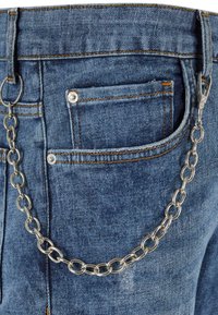 Jeans en denim bleu avec un accessoire en chaîne argentée attaché à la taille, des coutures orange contrastantes et une petite poche arrière.