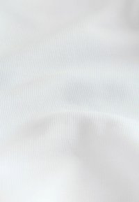 Gros plan d'un tissu blanc côtelé avec des plis doux et une texture visible.