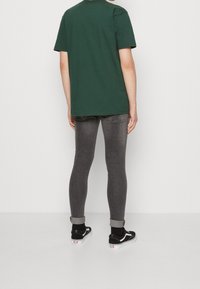 T-shirt en coton vert, à manches courtes, associé à un jean gris ajusté. Baskets noires avec des semelles blanches et un détail de revers.