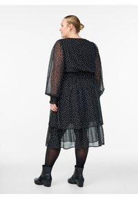 Melnas, punkotās, daudzslāņu kleitas ar caurspīdīgām garajām piedurknēm, elastīgu jostasvietu, vieglu audumu un potītes garuma apakšmalu, kas saskaņota ar melniem zābakiem.