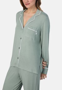 Lichtgroen, lange mouwen pyjama-top met een notch-kraag, witte bies en een enkele borstzak. Zacht materiaal met een relaxte pasvorm.