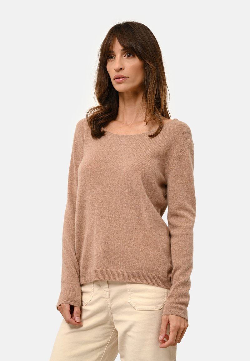 Hellbrauner, weicher Strickpullover mit rundem Halsausschnitt und langen Ärmeln. Mit gerippten Bündchen und Saum. Kombiniert mit cremefarbenen Hosen.