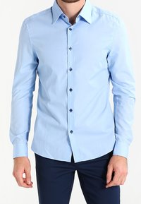 Ljusblå långärmad skjorta med en spetsig krage, prydd med mörkblå knappar och en slät, vävd textur. Skräddarsydd passform med en böjd nederkant.