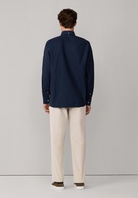 Camisa de manga larga azul marino con cuello abotonado, ajuste entallado y puños abotonados. Combinada con pantalones beige claros y zapatos informales.
