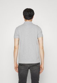 Polo gris de manga corta con cuello doblado, textura suave y dobladillo recto, combinado con jeans oscuros que presentan un sutil detalle en los bolsillos traseros.