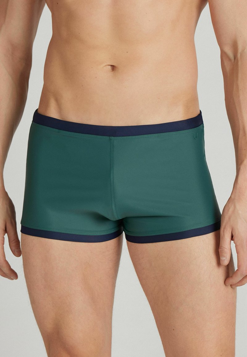 Grüne Schwimmshorts mit einem marineblauen Bund, körperbetontem Design und glatter Textur. Mit einer Länge bis zur Mitte des Oberschenkels, ausgestattet mit Doppelnähten entlang der Nähte.