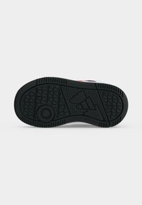 Semelle en caoutchouc noire d'une basket avec des motifs géométriques sur la bande de roulement et un logo Adidas embossé au centre.