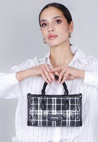 Borsa a sequins bianca e nera con motivo a quadri, forma strutturata, doppio manico e base nera lucida. Dettagli in metallo visibili.