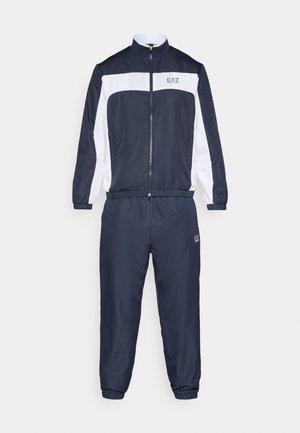 Laivastonsininen verkkatakki kevyestä kankaasta, jossa valkoinen raita rinnassa, vetoketjusuljenta sekä joustavat resorit ranteissa ja nilkoissa.