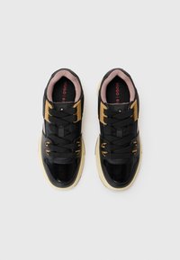 Black sneakers with gold accents, black laces, and glossy material. Features a padded pink lining and a textured sole.