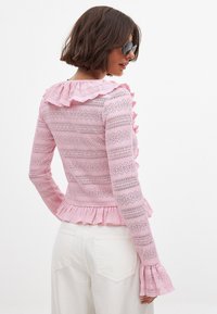 Rosa, texturerad tröja med volangkrage och ärmslut, med horisontella ränder. Peplumslut, långa ärmar, tillverkad av lätt material.