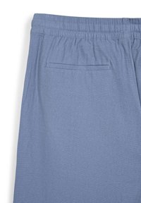 Hellblaue Hosen aus weichem Stoff, mit einem elastischen Bund und einer einzigen Gesäßtasche mit flacher Naht. Glatte Textur.