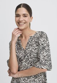 Svart och vit mönstrad blus med korta ärmar och V-ringning, med ett mjukt tyg och en avslappnad passform, som visar upp olika texturer.