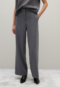 Grijze wijde broek met een soepele textuur, vlakke voorkant en zijzakken, gecombineerd met zwarte puntige enkellaarsjes.