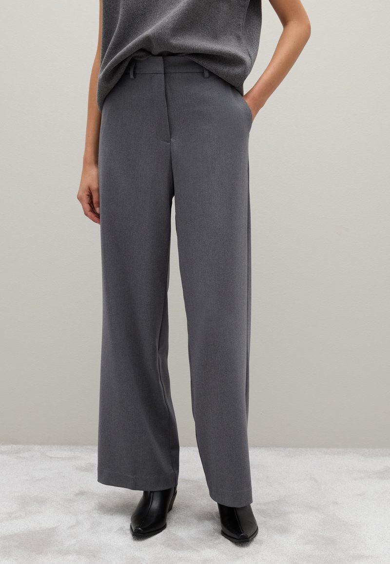Grijze wijde broek met een soepele textuur, vlakke voorkant en zijzakken, gecombineerd met zwarte puntige enkellaarsjes.