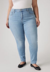 Ανοιχτό μπλε στενά τζιν με ψηλή μέση, διαθέτουν θηλιές για ζώνη, πίσω τσέπες και λεία υφή. Φορεμένα με μαύρα μπαλέτα.