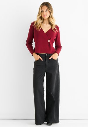 Bordeaux wikkeltrui met een decoratieve knoop, gecombineerd met hooggewaisted zwarte brede jeans. Zachte textuur en een getailleerd ontwerp.