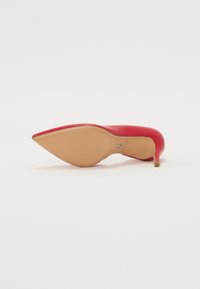 Escarpin en cuir rouge à bout pointu et petit talon fin, vu de la semelle sur fond blanc.