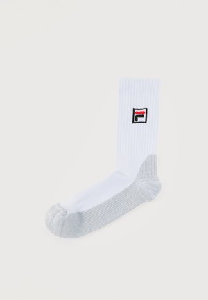 Chaussette blanche côtelée avec talon et orteils gris et une petite écusson logo aux couleurs rouge, blanc et noir.