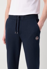 Tute blu navy realizzati in tessuto morbido, dotati di vita elasticizzata con cordino, tasche laterali e un logo circolare Colmar.