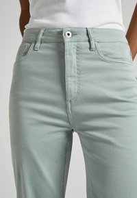 Light green cotton-blend pants with a slim fit, featuring a front zipper, button closure, and standard pockets. Smooth texture.