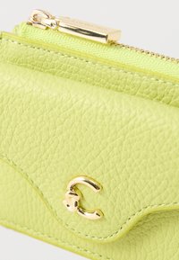 Vihreä nahkalompakko, jossa on teksturoitu pinta, kultainen vetoketju ja metalliosat. Siinä on kaareva läppä ja koristeellinen kultainen tunnus.