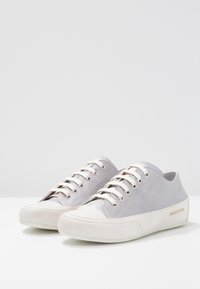 Šedé semišové tenisky s bílou gumovou podrážkou, mají ploché šňůrky a kovové okovy, značkový akcent na boku. Hladký povrch a nízký profil.