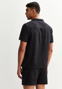 Men's black short-sleeve shirt and matching shorts made of textured fabric. Features a collar and a back yoke detail.
