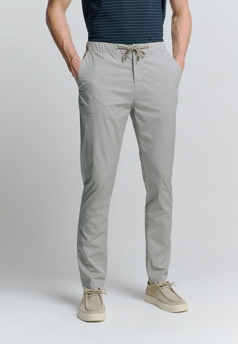 Lichtgrijze, stretch stof broek met een elastische tailleband en verstelbaar aantrekkoord. Voorzien van zijzakken, taps toelopend ontwerp en een zachte textuur.