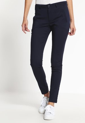 Marineblauwe broek met een slanke pasvorm, gemaakt van rekbaar materiaal. Met knoopsluiting, voorzakken en taps toelopende benen. Gepaard met witte sneakers.