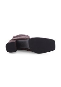 Braune Wildlederstiefel bis zum Knie mit einem klobigen Absatz und einer abgerundeten Spitze. Die Sohle ist schwarz und flach mit einem strukturierten Muster für besseren Halt.