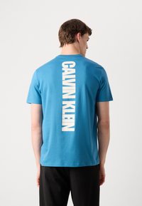 T-shirt in cotone blu con logo bianco "CALVIN KLEIN" verticale sul retro. Maniche corte e design a girocollo.