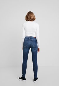 Höga blå jeans med smal passform, denimmaterial och två bakfickor. Matchas med en vit långärmad skjorta och svarta sneakers.