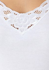 Witte geribde tanktop met een bloemenkantafwerking bij de halslijn, die ingewikkelde details en een zachte textuur laat zien.